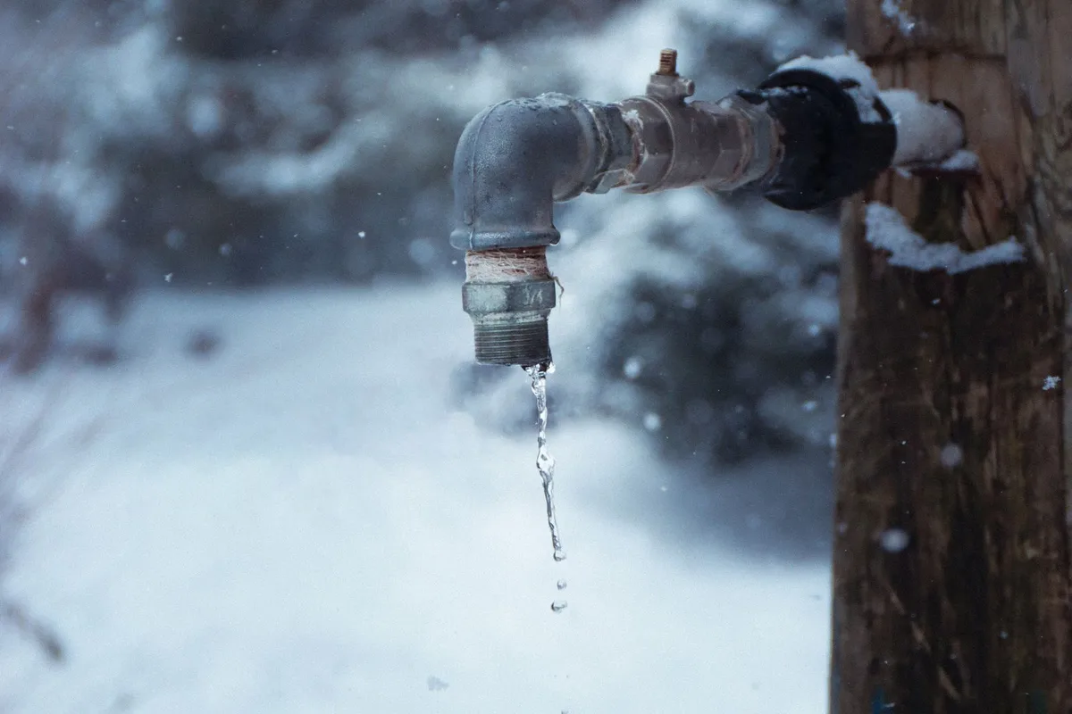 A frozen outdoor faucet dripping in the snow during a Sherman, TX hard freeze