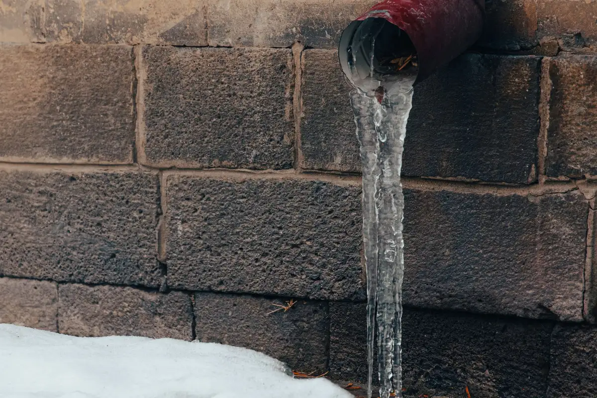 Ice hanging from a frozen pipe against a stone wall in Sherman, TX